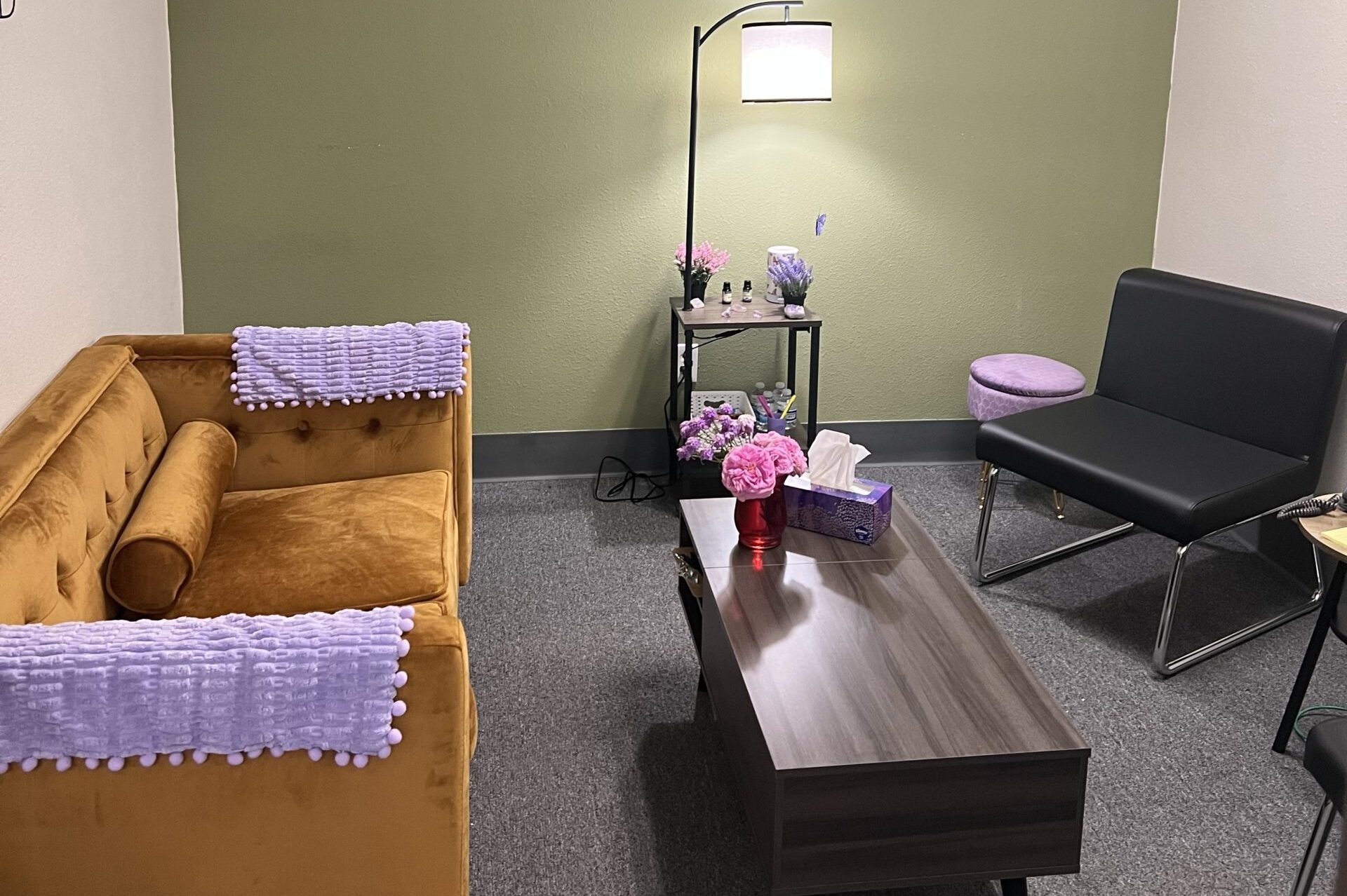 A visiting room has a green wall, a gold sofa and a standing light, lit.