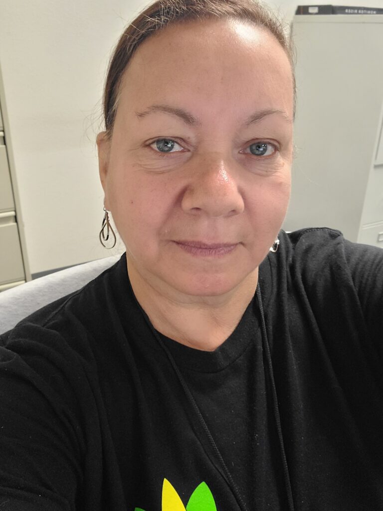 Maria looks steadfastly at the camera. Her hair is pulled back and she wears a black Family Justice t-shirt and silver earrings. 